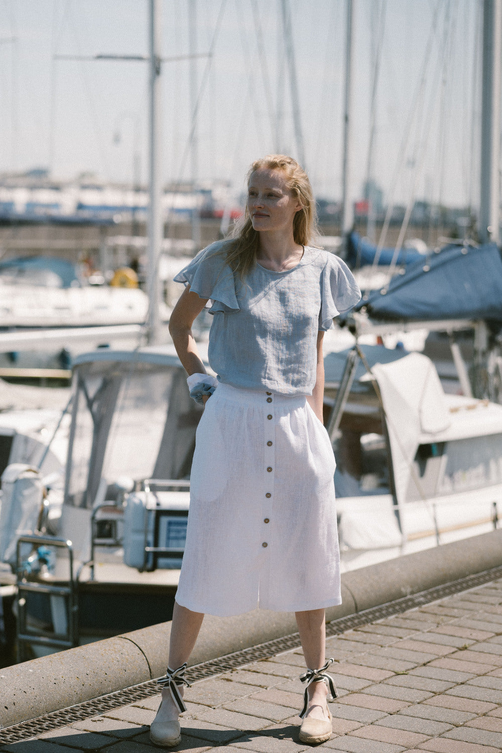 Woman wearing a light blue gauze linen top with flutter sleeves by the marina